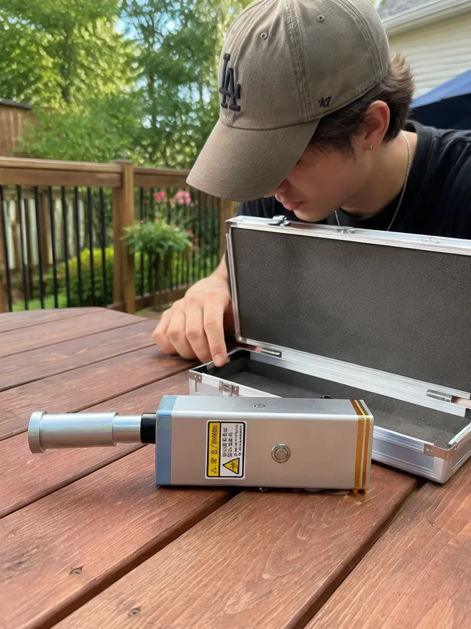 KyberSpark Core V2 on a wooden outdoor table beside the open aluminum-alloy box in natural daylight, barrel facing left, metal body visible