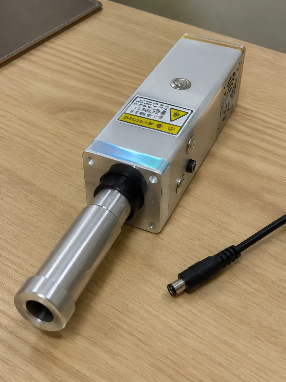 KyberSpark Core V2 on a desk with the barrel end facing the camera and a dedicated charger cable visible to the side, soft indoor light suggesting a charging context