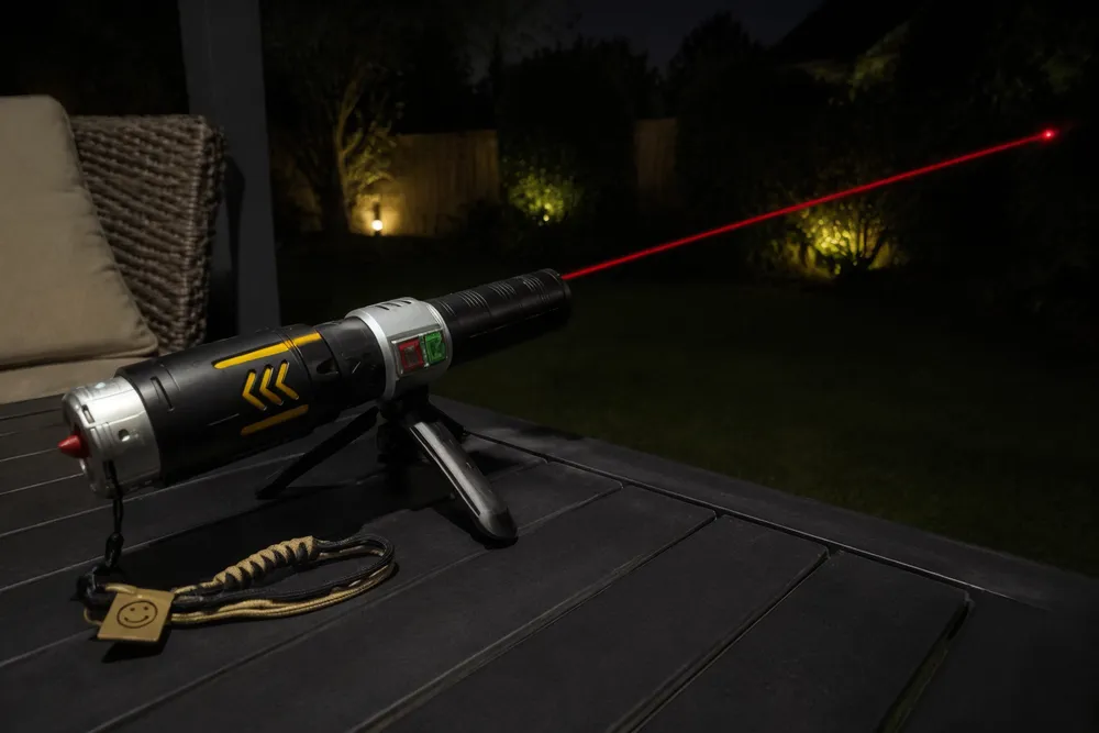 KyberSpark X held outdoors at night with a faint red beam visible extending into the dark, person's hand and alloy body readable in low light