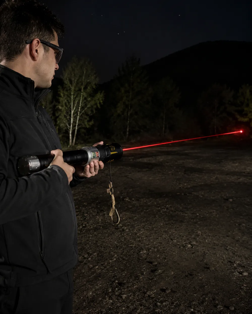 KyberSpark X held at night with thin red laser beam visible extending across a dark outdoor environment